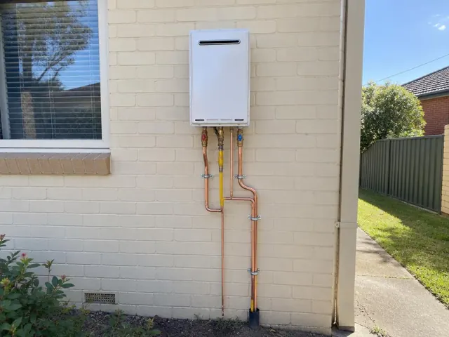 Wall-mounted hot water unit with copper pipework on a brick exterior wall in Matraville