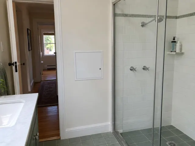 Small access panel on a painted bathroom wall beside a shower in Kensington